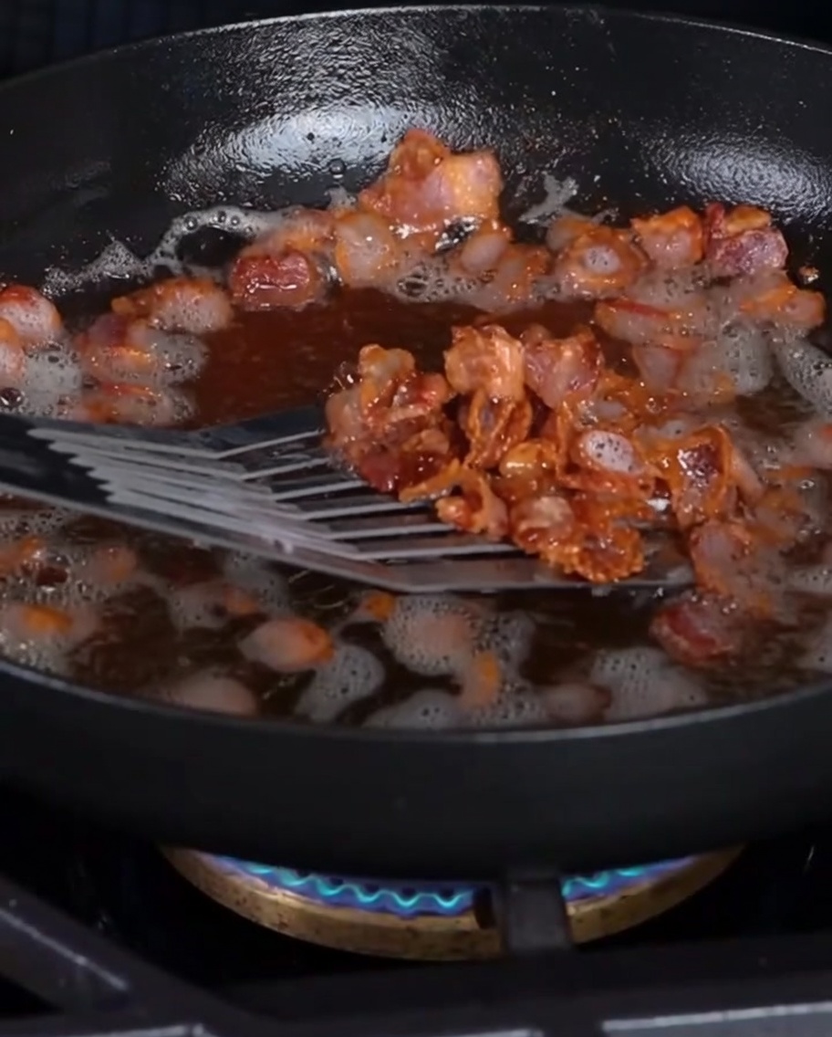 Knusprige Baconstückchen werden mit einem Schaumlöffel aus der Pfanne gehoben.