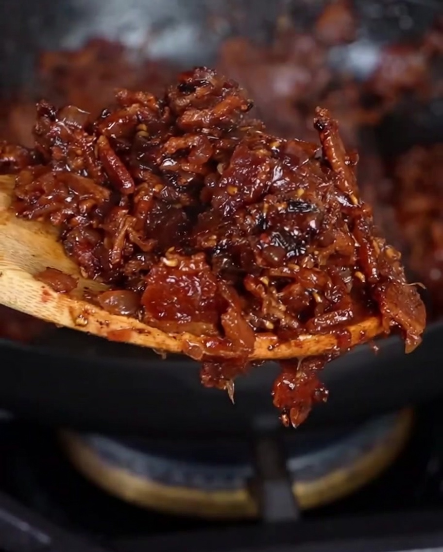 Ein Holzlöffel hebt eine Portion dicker, dunkelrot-brauner selbstgemachter Bacon Jam an.
