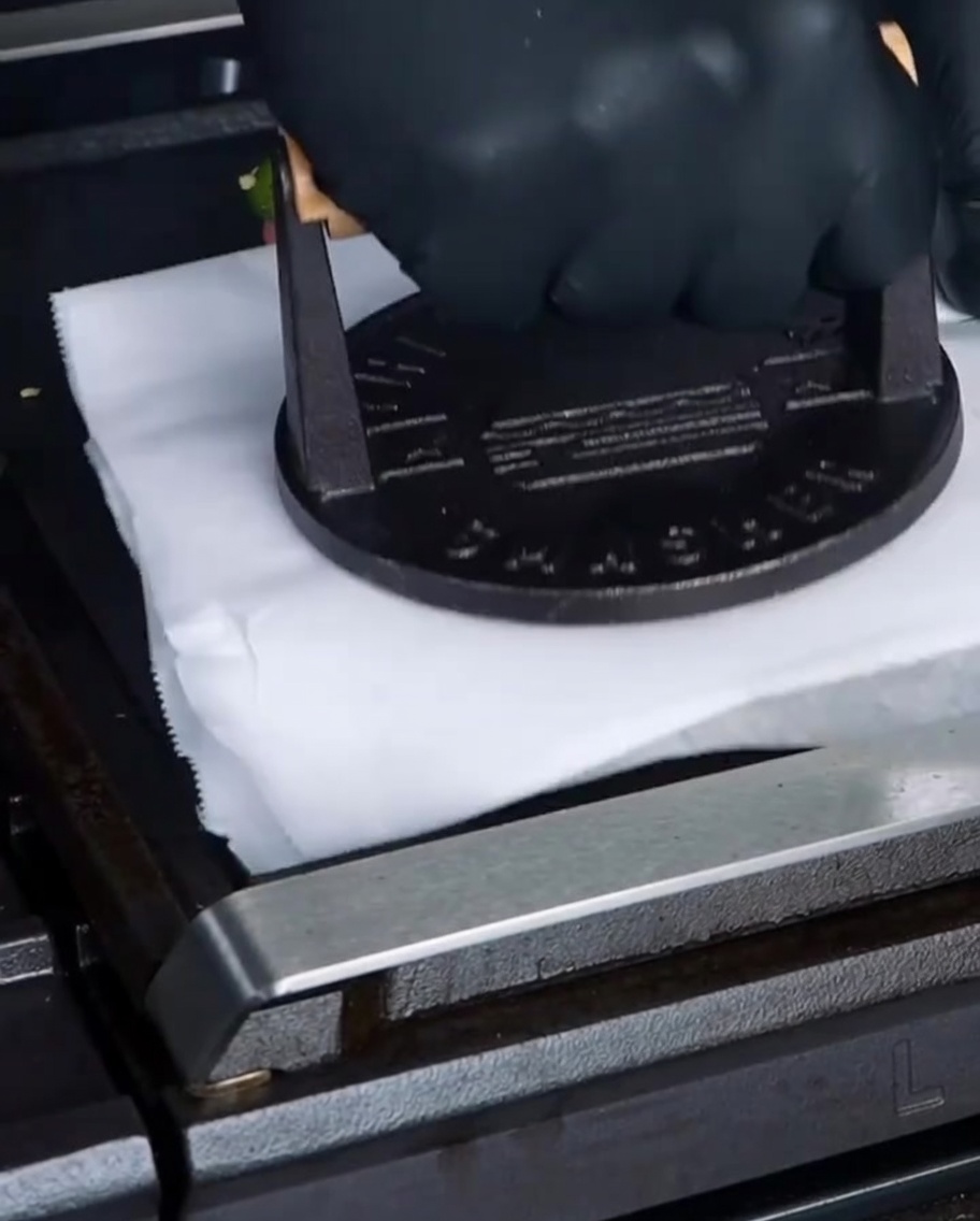 Eine schwere gusseiserne Burgerpresse drückt über einem Stück Backpapier ein Rindfleisch-Patty auf der Grillplatte platt.