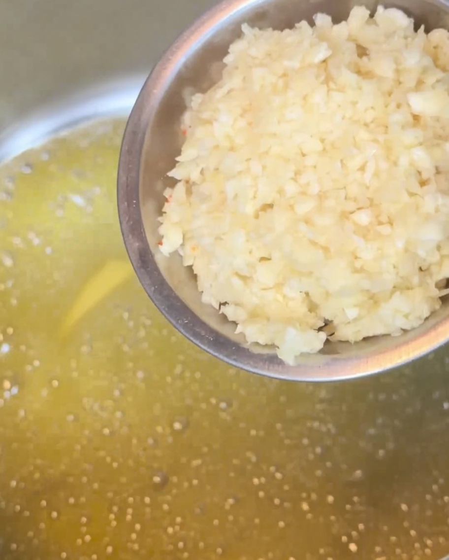 Gehackter Knoblauch brutzelt in schmelzender Butter in einem Metalltopf und wird goldbraun.