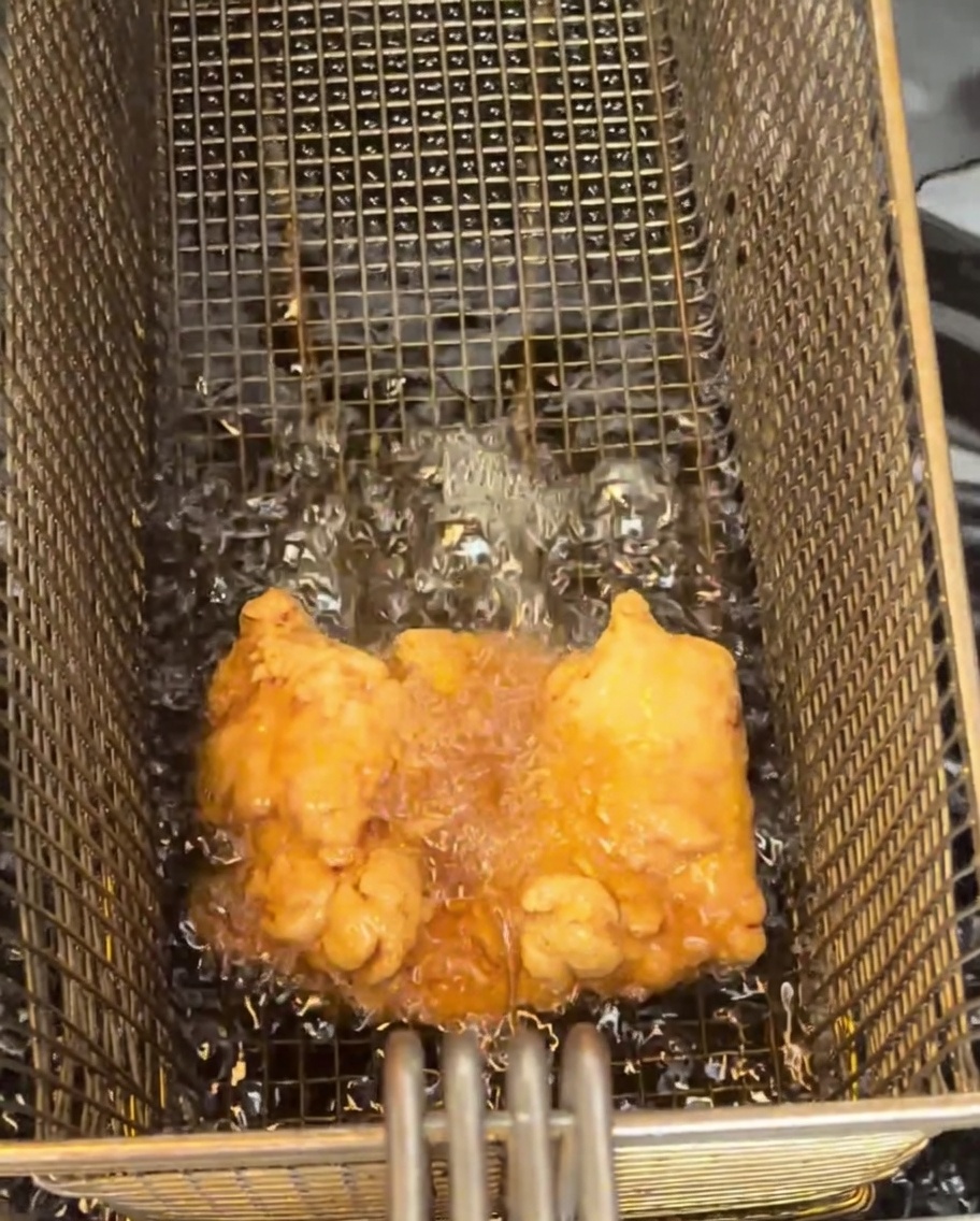 Ein goldbraun gebratenes Hähnchenschenkel-Filet liegt auf einem Drahtgitter.