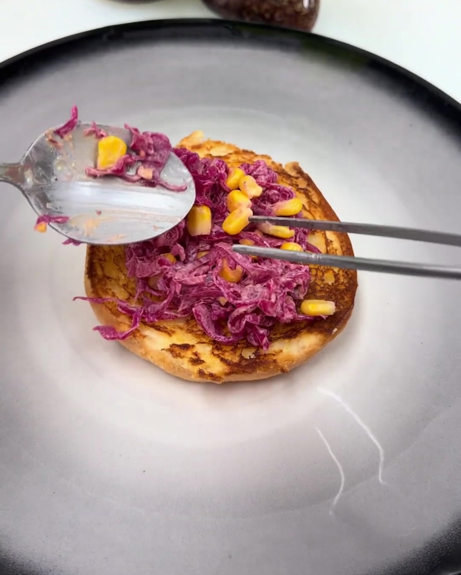 Ein glänzend glasiertes Hähnchenfilet ruht auf dem Rotkohlsalat auf dem Brötchen.