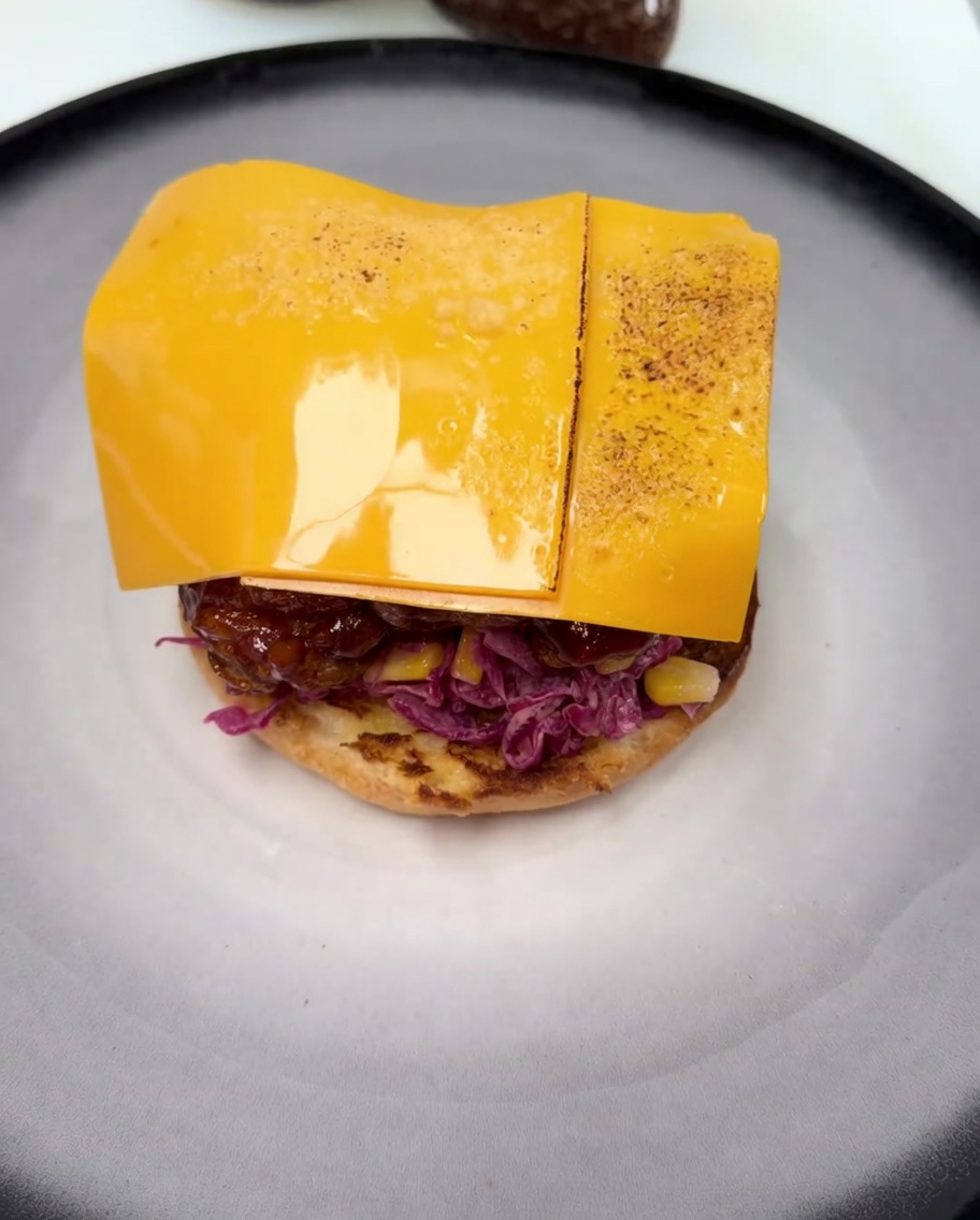Eine Scheibe Cheddar schmilzt auf dem glasierten Hähnchen, mit leichten Bräunungsspuren vom Flambieren.