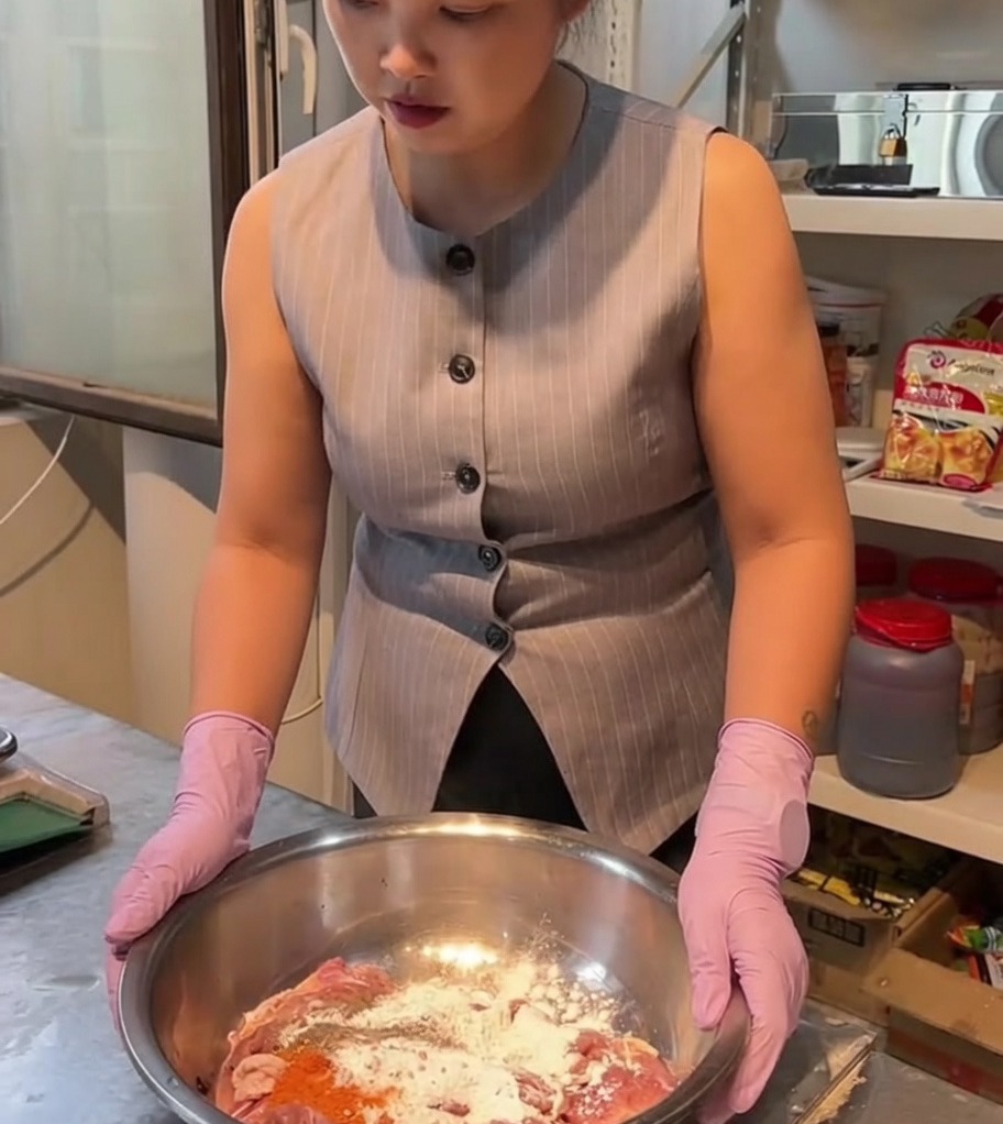 Rohe Hähnchenstücke werden in einer großen Edelstahlschüssel mit Gewürzen und Marinade vermischt.