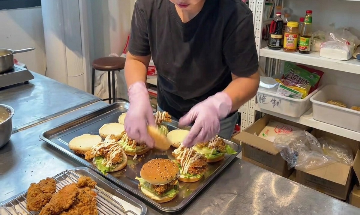 Eine Person setzt die obere Brötchenhälfte auf einen fertig zusammengebauten Burger.