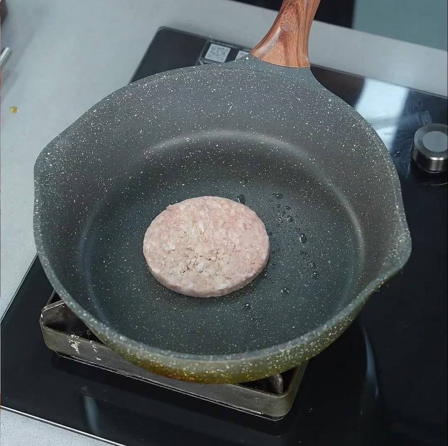 Ein rohes Rindfleisch-Patty brutzelt in einer leicht geölten Pfanne auf dem Herd.