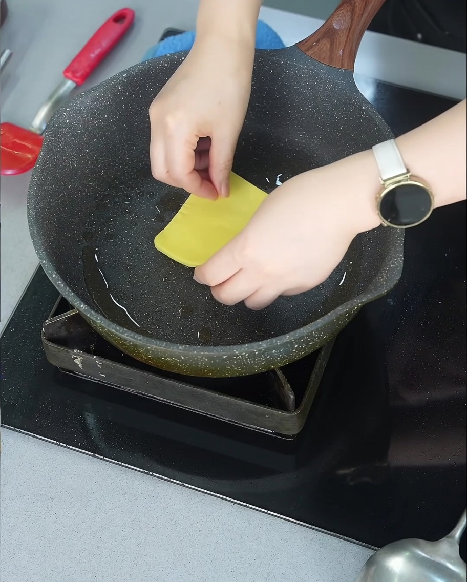 Eine Scheibe gelber Käse schmilzt über einem gebräunten Rindfleisch-Patty in einer Bratpfanne.