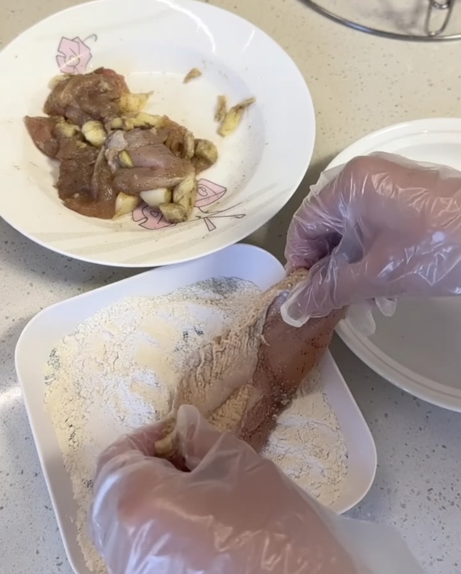 Hähnchenstücke werden in eine Panade auf einem weißen Teller gedrückt.