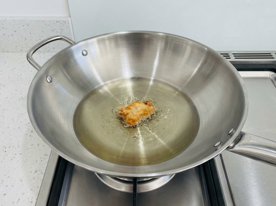 Ein Stück paniertes Hähnchen brät in einem Wok mit heißem Öl.
