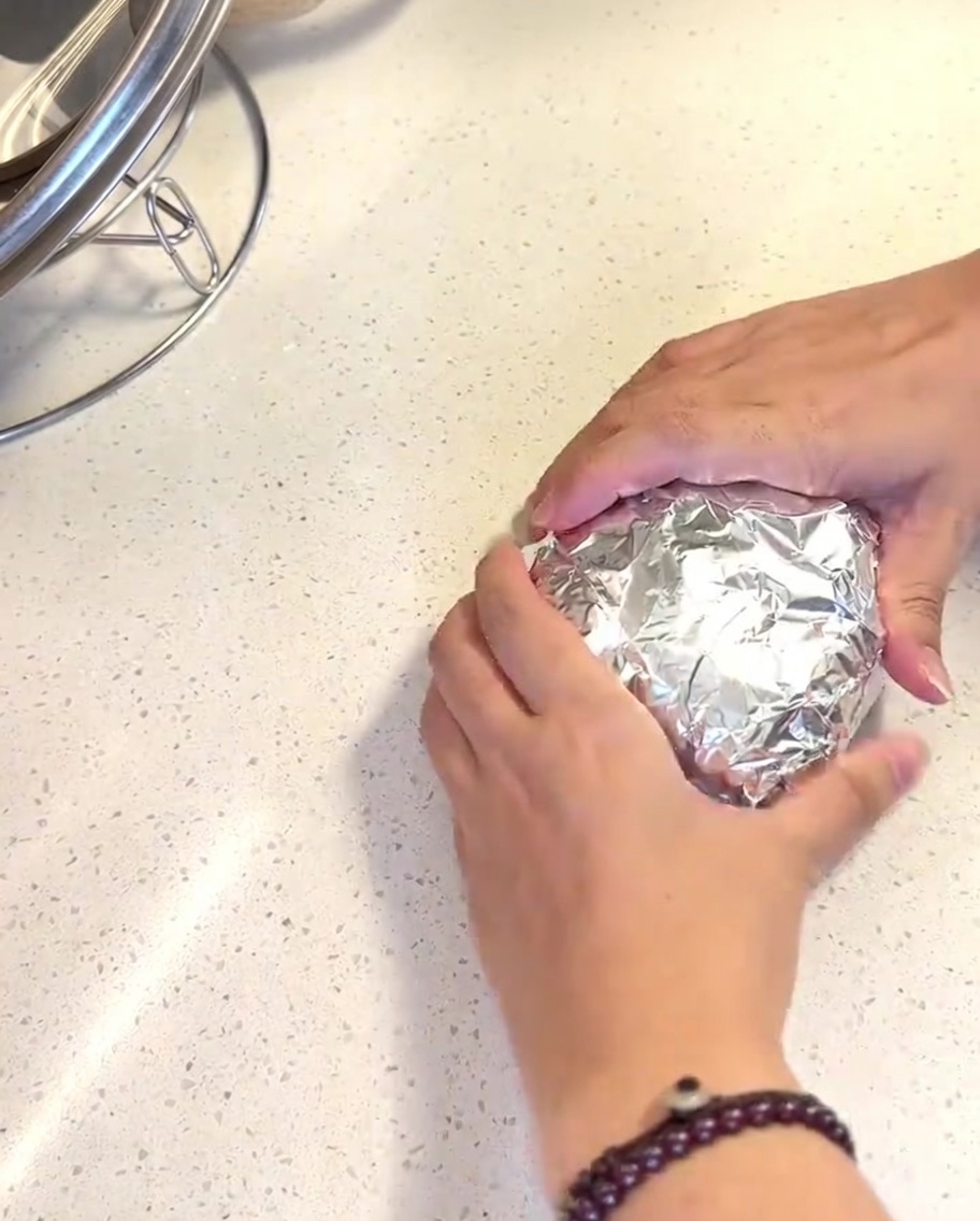 In Alufolie gewickelte Hamburger-Brötchen im Korb eines Airfryers.