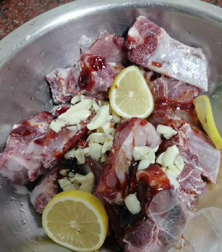 Rohe Schweinerippchen vermischt mit dunkler Marinade, Knoblauch und frischen Zitronenscheiben.