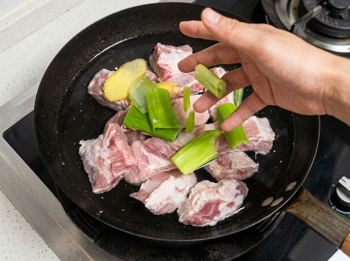 Schweinerippchen, Ingwer und Frühlingszwiebeln in einem Topf mit kaltem Wasser.