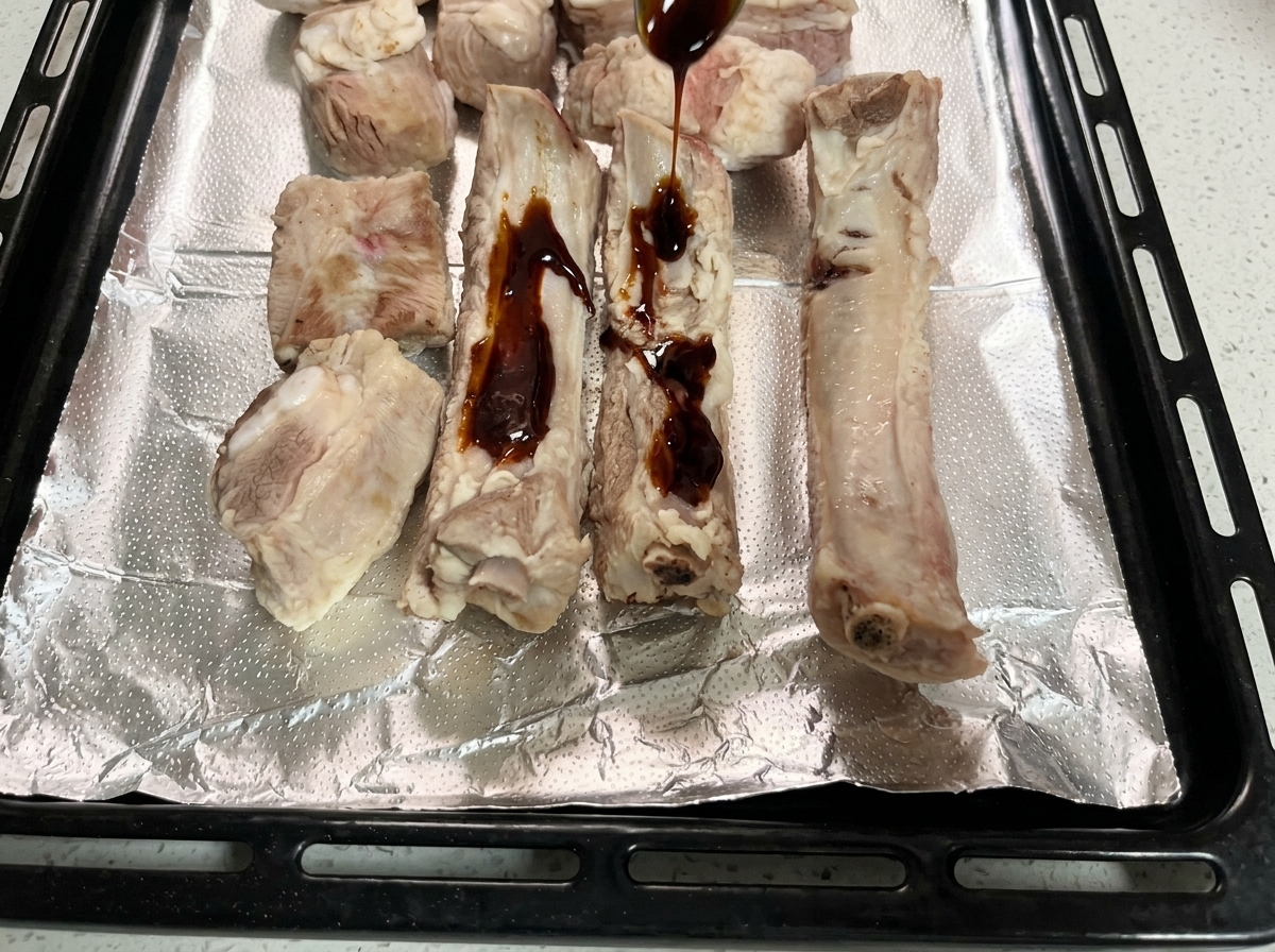 Dunkle Marinade wird über die rohen Rippchen auf dem Backblech gegossen.