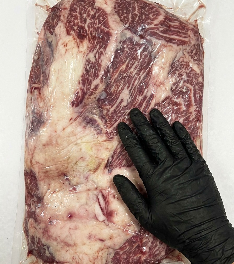 Eine Nahaufnahme eines Messers, das das dicke, überschüssige Fett von einem rohen Stone Axe Wagyu Brisket entfernt.