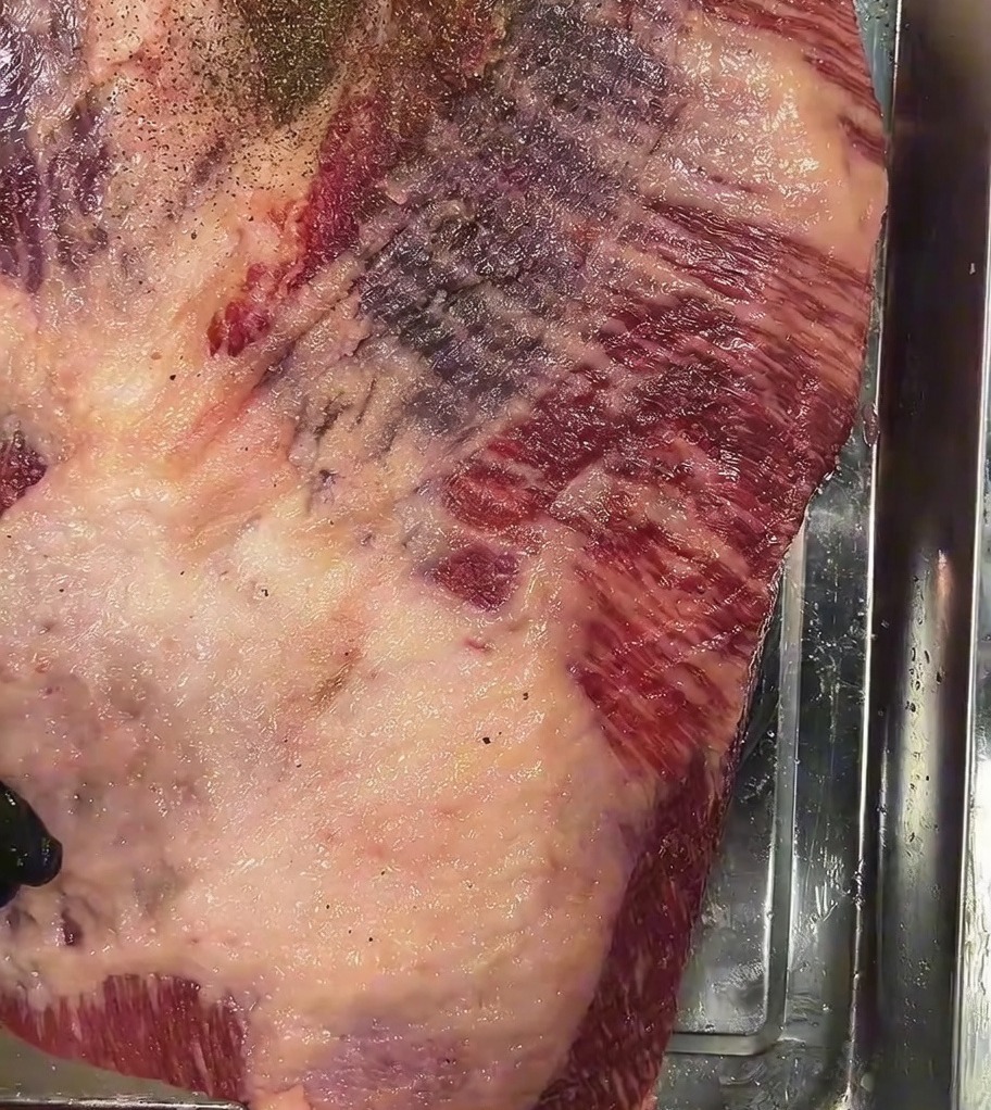 Grober schwarzer Pfeffer wird großzügig über die Oberseite des gesalzenen rohen Briskets gestreut.