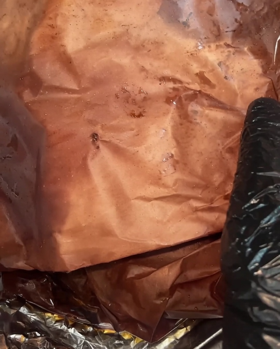 Das vollständig gegarte Brisket ist ausgepackt und zeigt eine dunkle, feuchte Kruste sowie reichlich Säfte, die sich im Metzgerpapier sammeln.