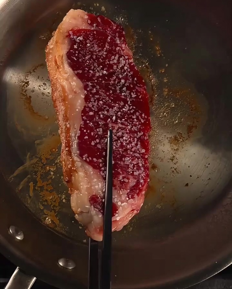 Steak in der Pfanne wird mit Butter, Knoblauch und frischen Rosmarinzweigen begossen.