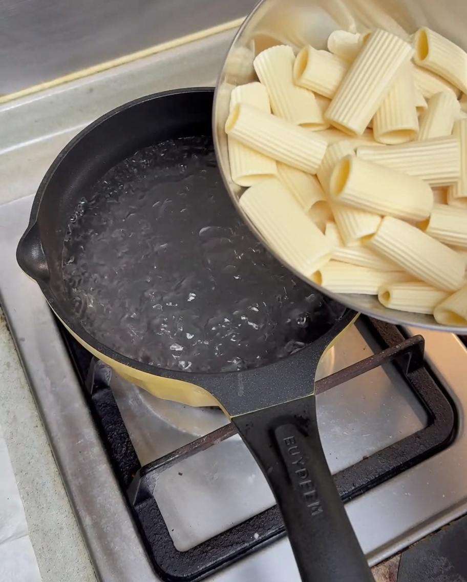 Über Nacht eingeweichte Rigatoni werden aus einer Schale in kochendes Wasser in einem Topf auf einem Gasherd gegeben.