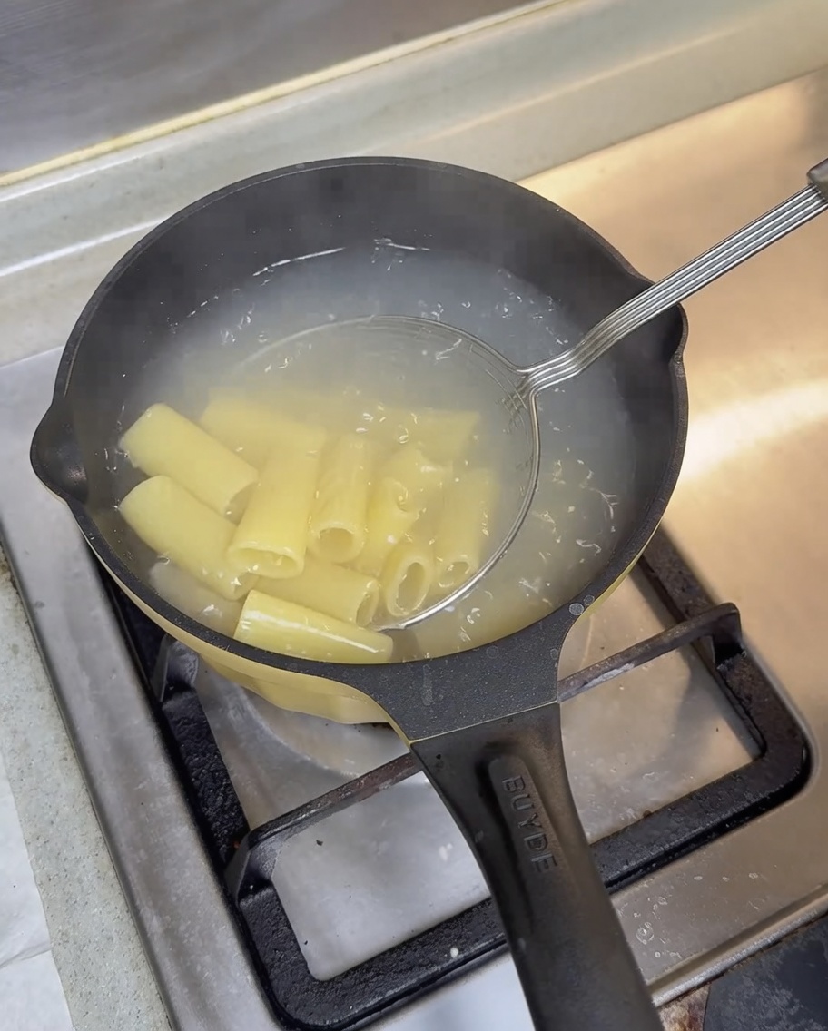 Gekochte Rigatoni werden mit einem Sieblöffel aus dem kochenden Wasser gehoben.