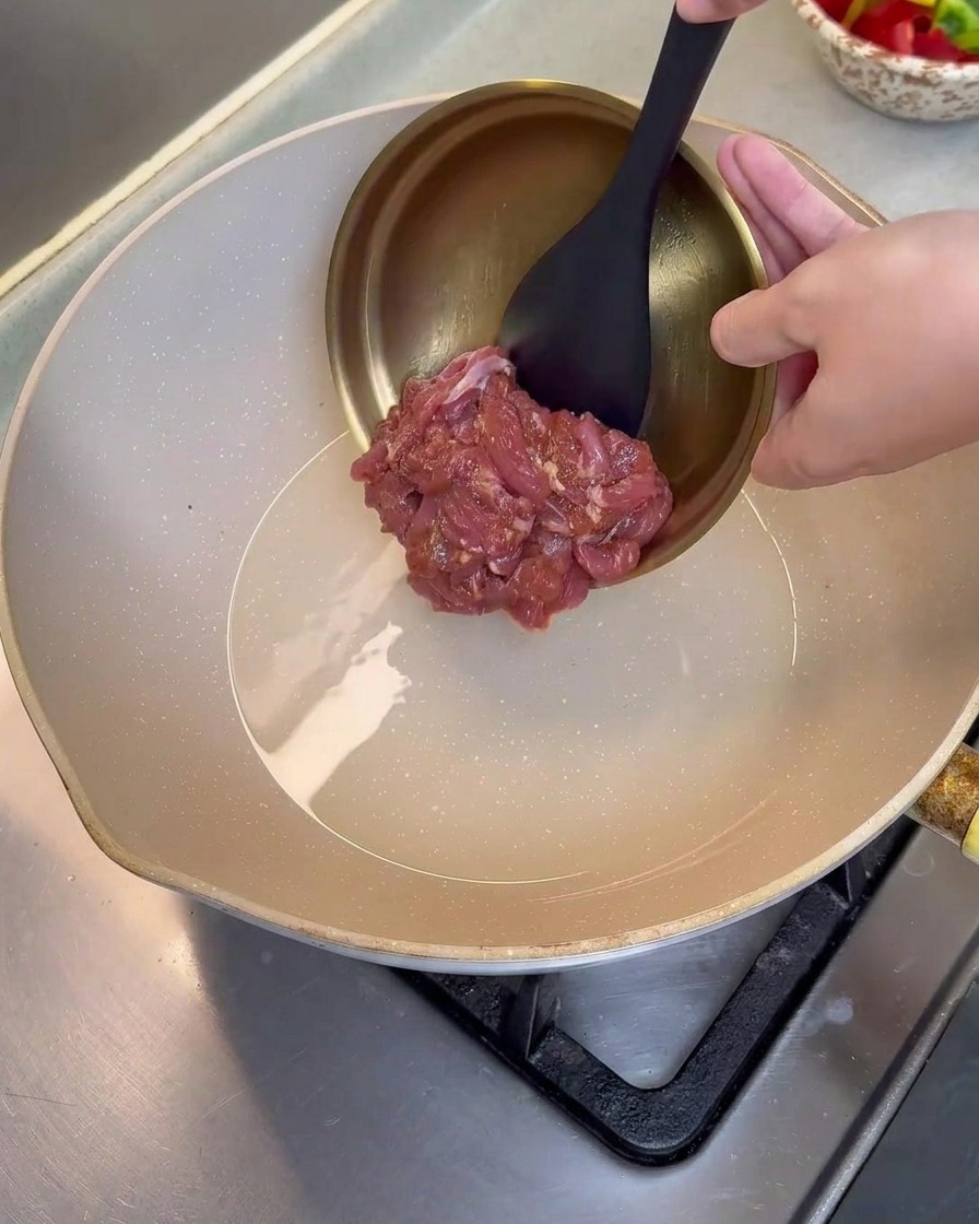 Marinierte Schweinefleischstreifen werden in eine heiße, geölte Pfanne gegeben.