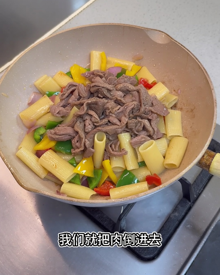 Gebratenes Fleisch und eine dunkle Sauce werden zu der Pasta und dem Gemüse in der Pfanne gegeben.
