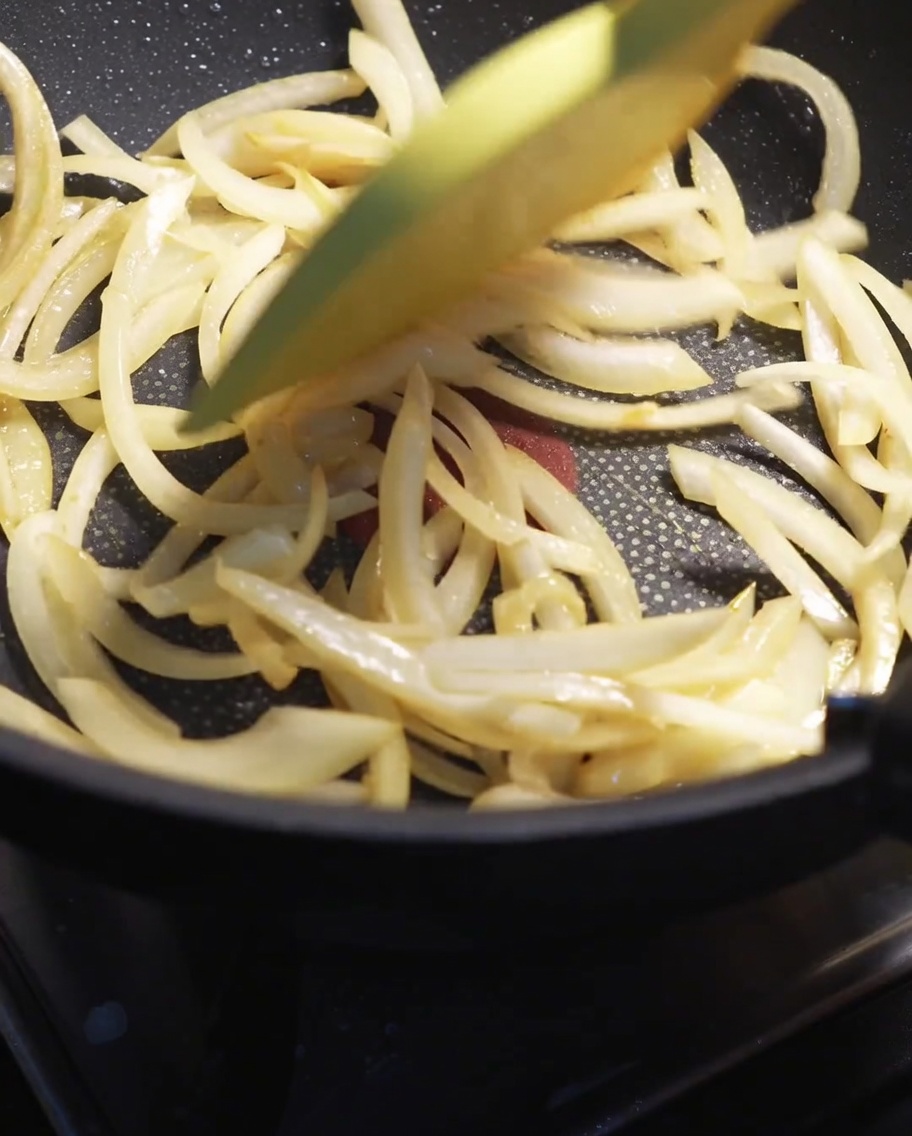 Zwiebelstreifen werden mit einem Pfannenwender in einer heißen Pfanne weich gebraten.