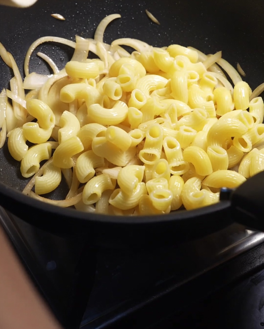 Gekochte Makkaroni-Röhrchen werden in eine Pfanne mit weich gebratenen Zwiebeln gegeben.