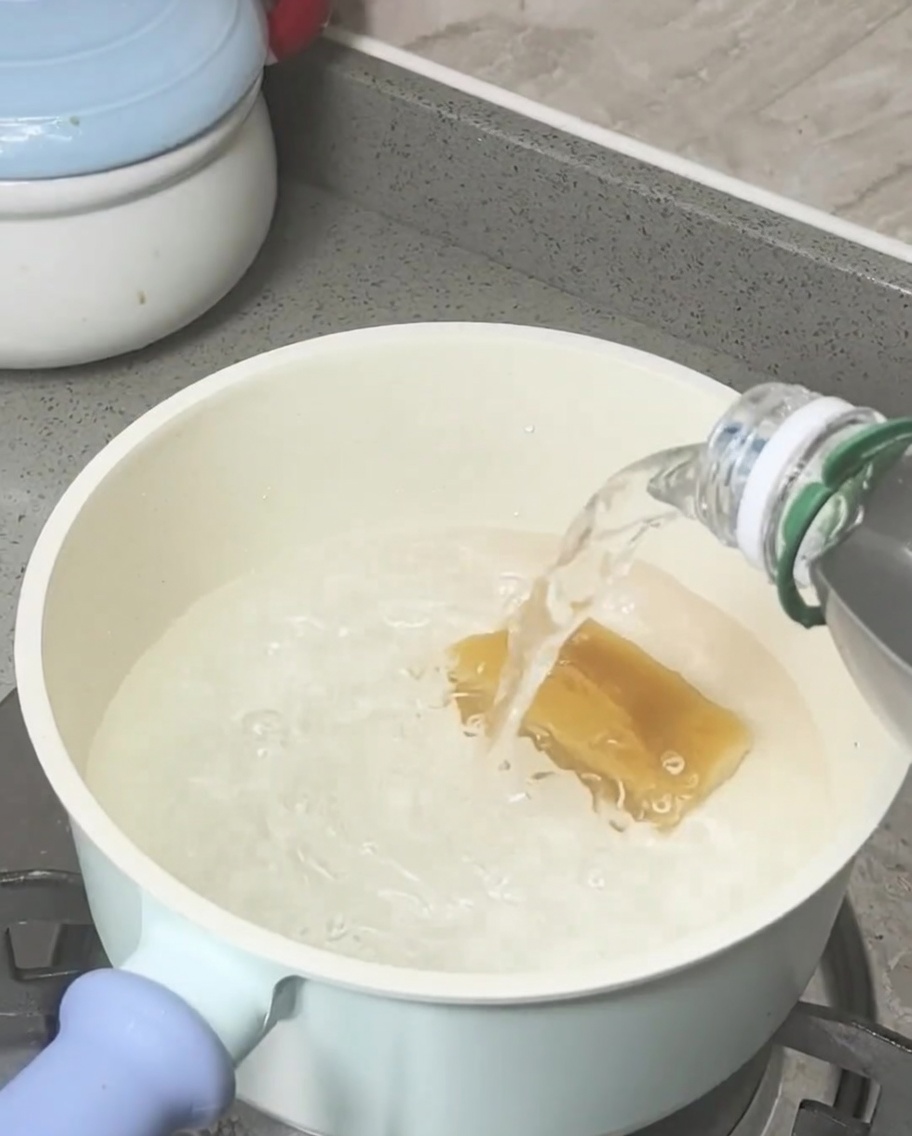 Ein Block brauner Zucker schmilzt in kochendem Wasser in einem hellen Topf.