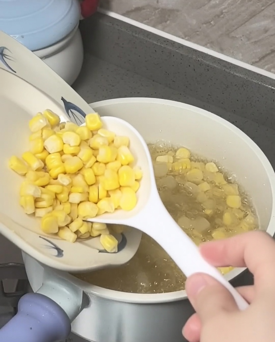 Maiskörner und zerkleinerte Wasserkastanien werden in den Topf mit kochendem Zuckerwasser gegeben.