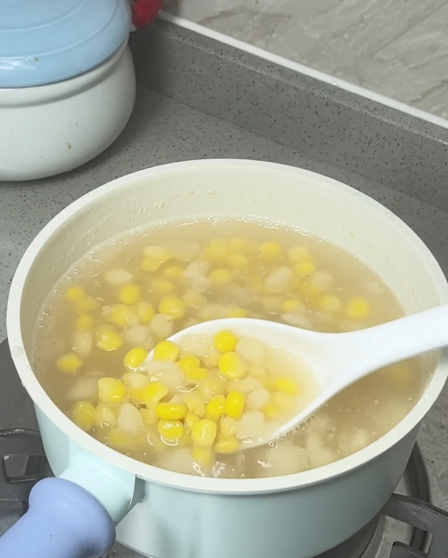 Kokosmilch wird über die fertige Mais- und Wasserkastaniensuppe im Topf geträufelt.