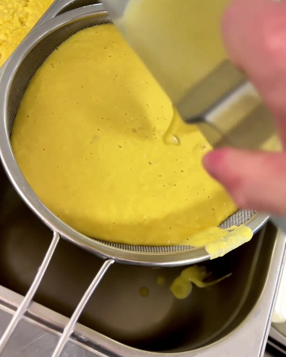 Maissuppe wird durch ein feines Sieb in einen Behälter gestrichen.