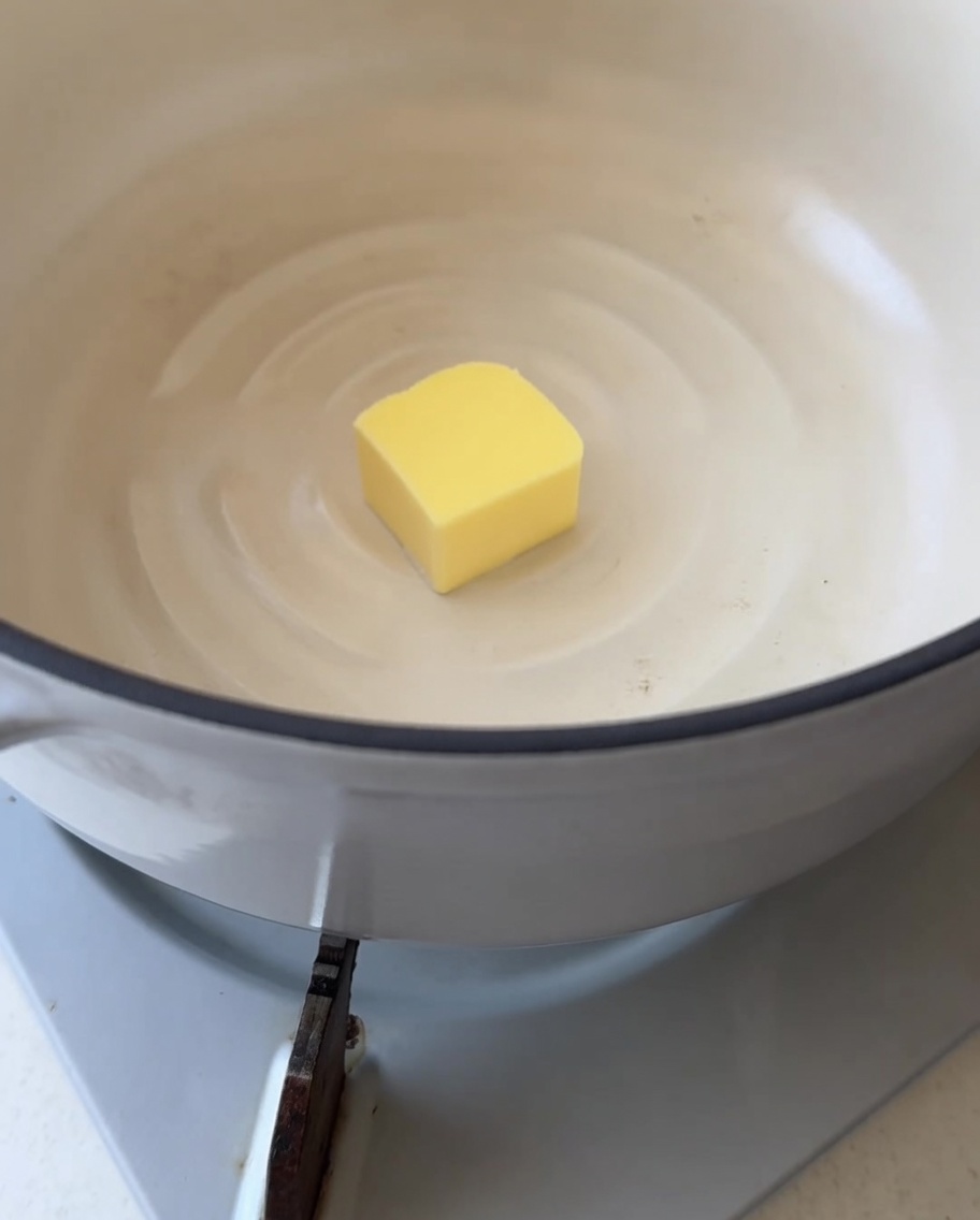 Nahaufnahme eines einzelnen Butterstücks, das in einem sauberen weißen Topf zu schmelzen beginnt.