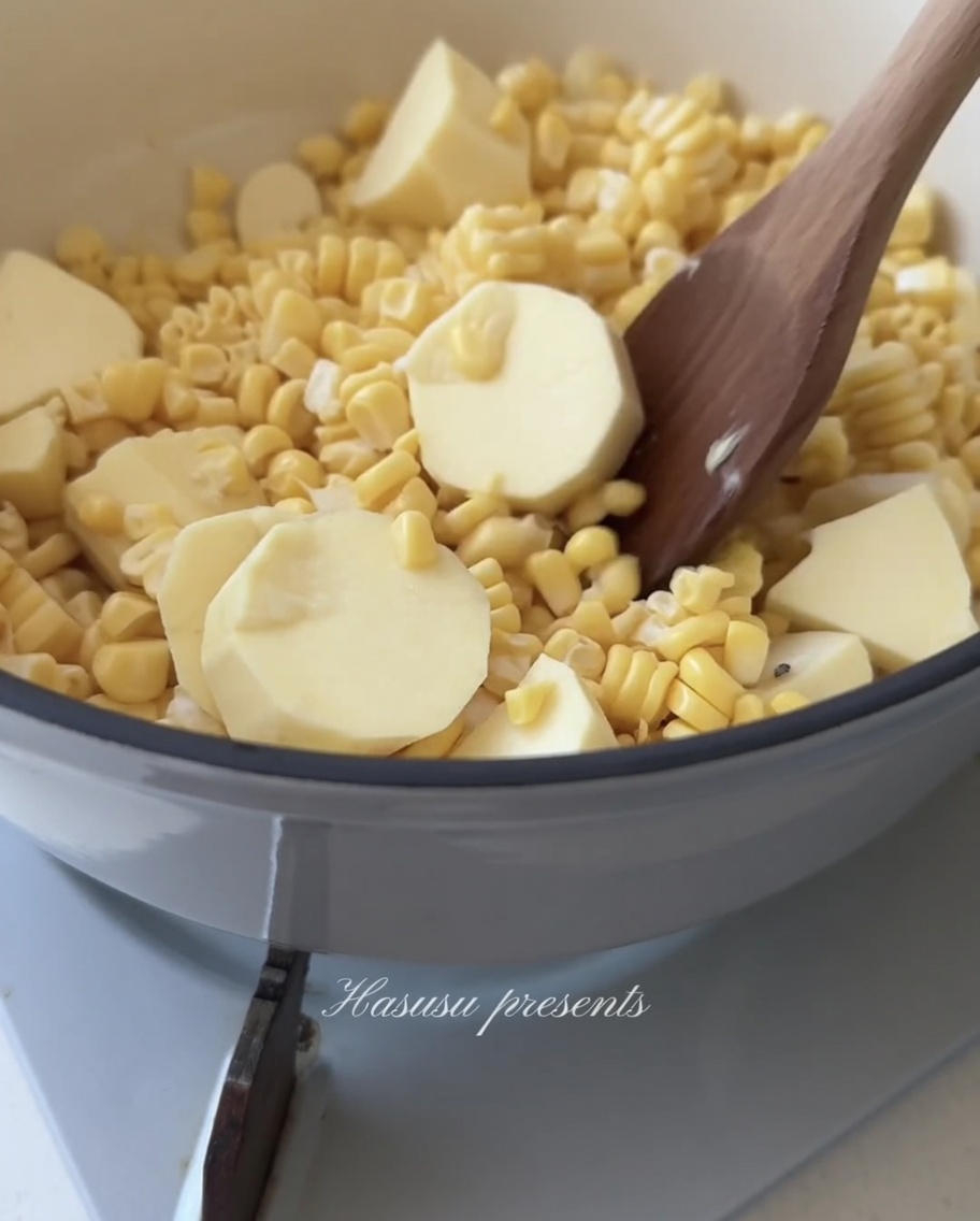 Ein Holzlöffel rührt eine Mischung aus gelben Maiskörnern und weißen Süßkartoffelstücken in einem Topf um.
