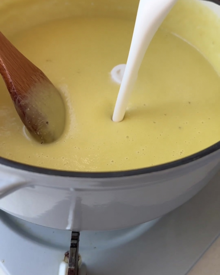 Weiße Sahne wird in einen Topf mit glatter, hellgelber Maissuppe gegossen.