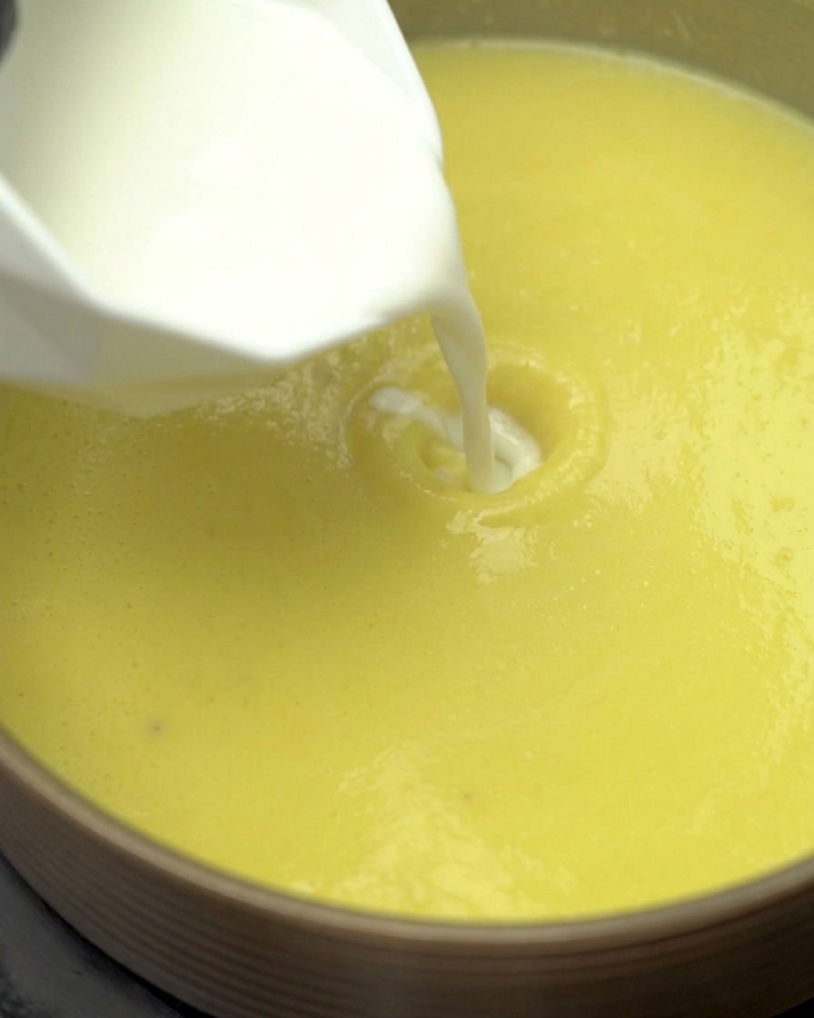 Milch und leichte Sahne werden in die köchelnde Mais-Suppenbasis gegossen.