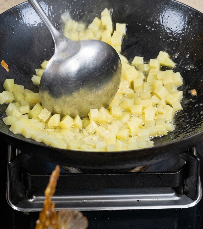 Gewürfelte Kartoffeln werden im Wok mit Öl angebraten, bis sie leicht gebräunt sind.