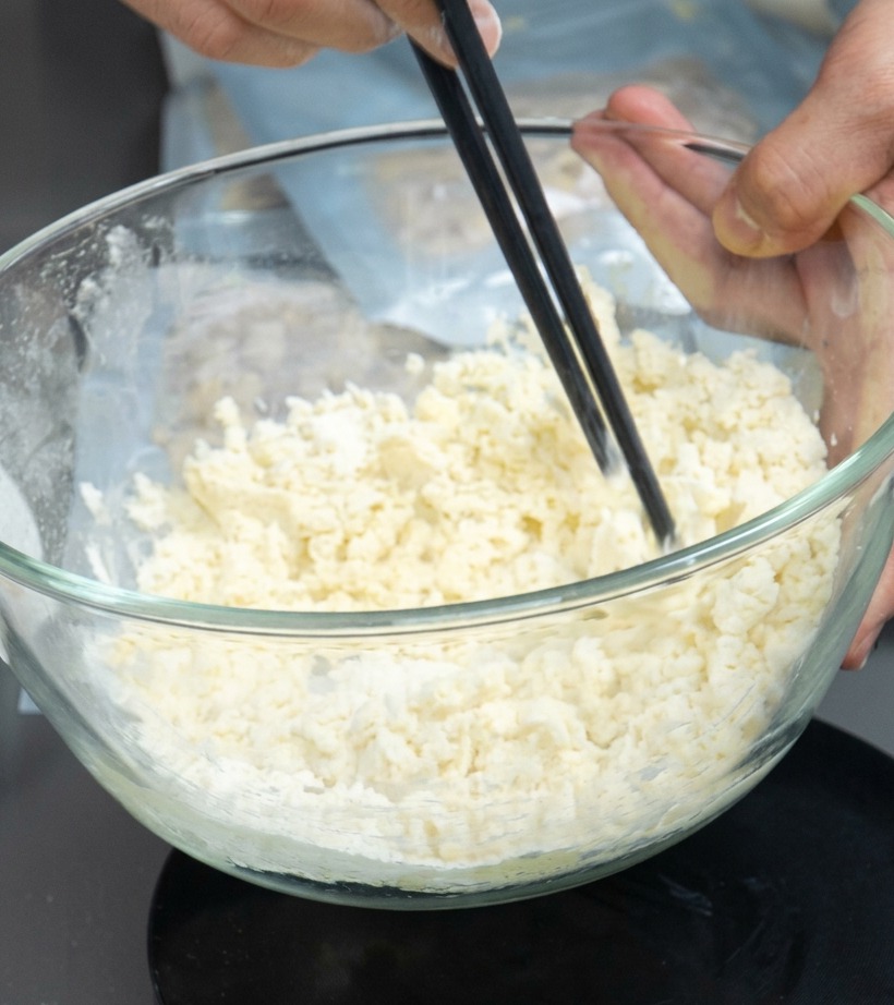 Eine Schüssel mit Mehl-Ei-Mischung, die mit Stäbchen zu Krümeln verrührt wird.