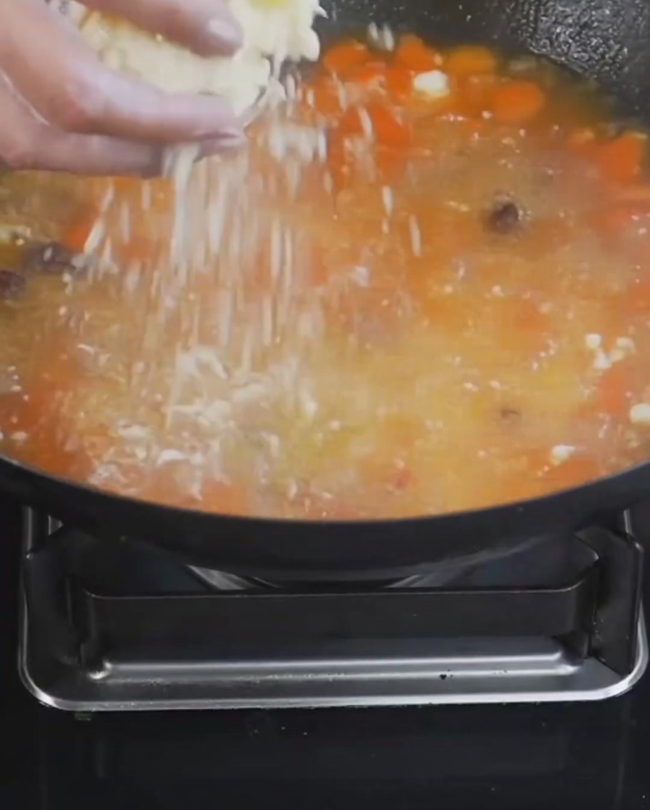 Mehl-Ei-Klößchen werden in eine köchelnde Suppe mit Tomaten und Kartoffeln gestreut.