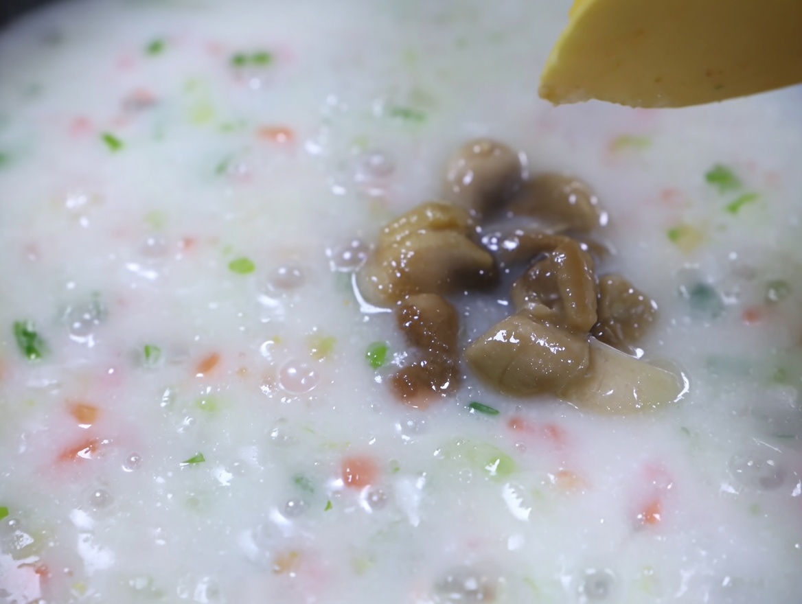 Gekochtes Muschelfleisch wird in eine köchelnde, cremige Gemüsesuppe gegeben.