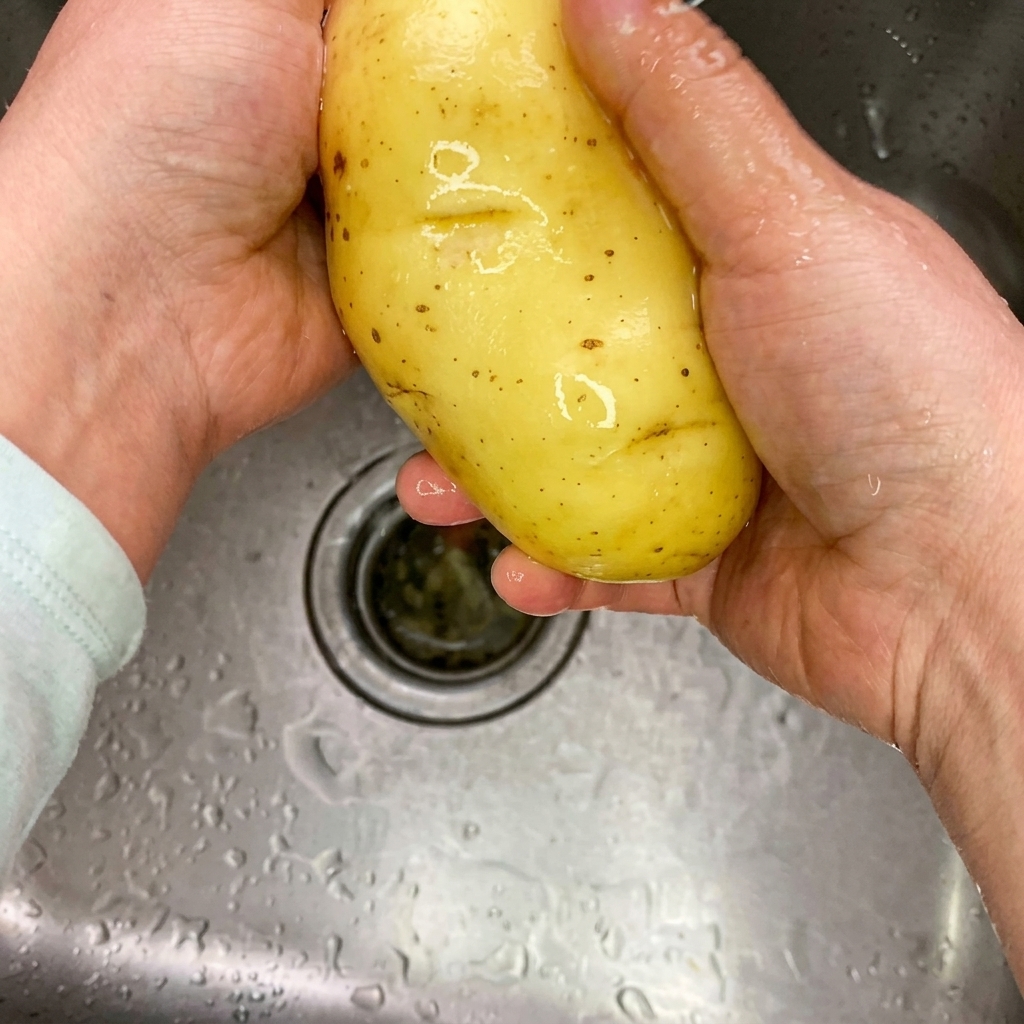 Dünn geschnittene, rohe Kartoffelstreifen auf einem sauberen Holzschneidebrett.