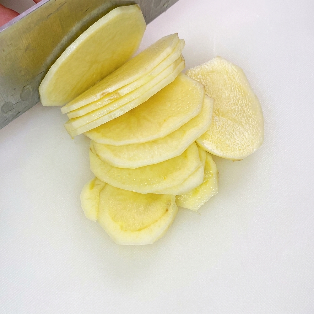 Gleichmäßig geschnittene, dünne Kartoffelstreifen auf einem weißen Schneidebrett.