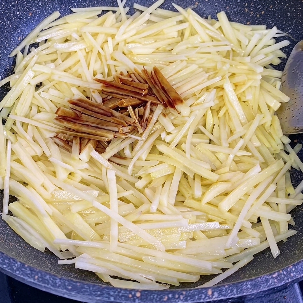 Sojasauce und Austernsauce werden über die bratenden Kartoffelstreifen im Wok gegeben.