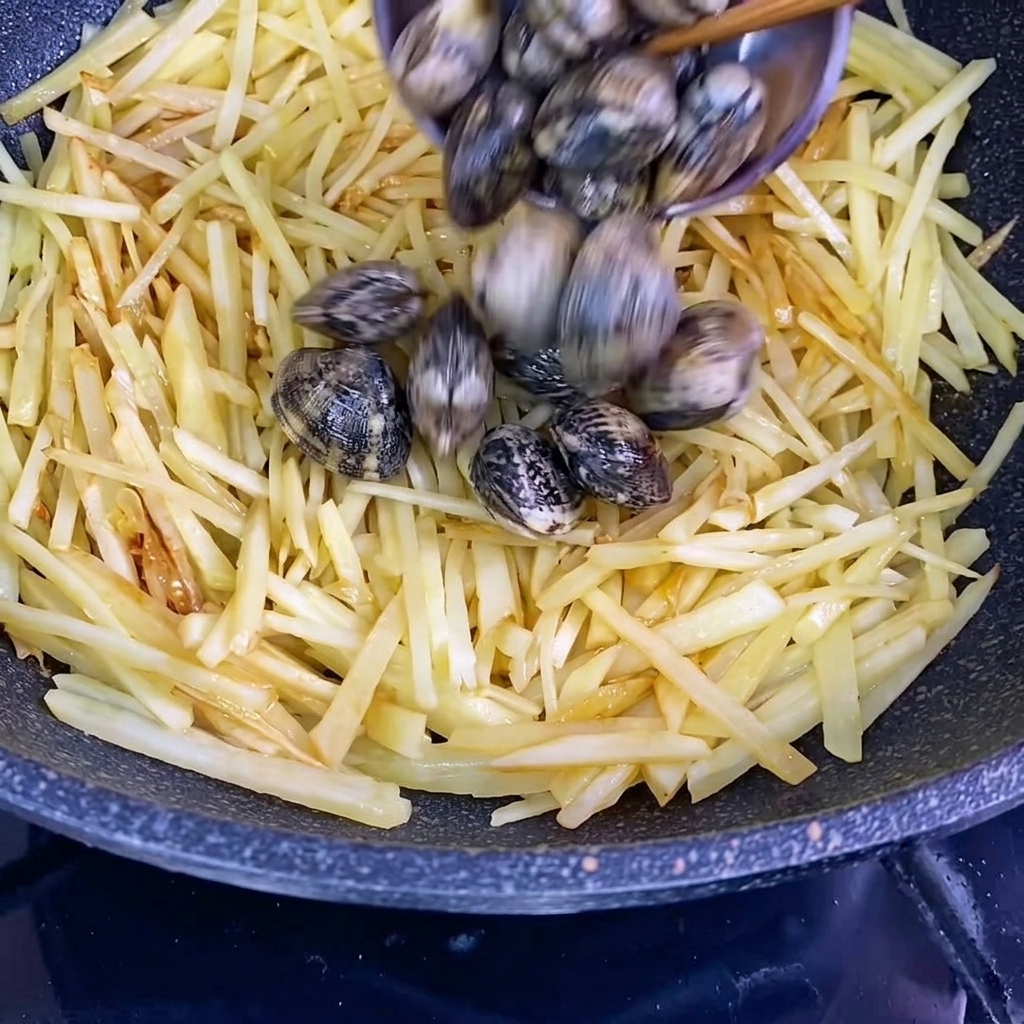 Frische Muscheln in Schale werden zu den gewürzten Kartoffelstreifen in den Wok gegeben.