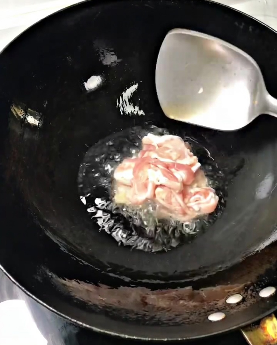 Dünne Schweinefleischscheiben braten in einem heißen Wok mit Öl und werden mit einem Metallspatel gewendet.