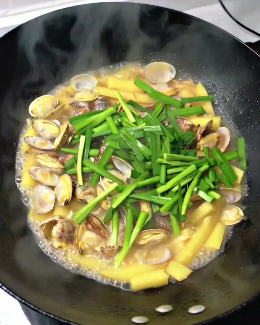Gehackter frischer Knoblauch-Schnittlauch wird über die Muscheln, Kartoffeln und das Schweinefleisch gestreut.