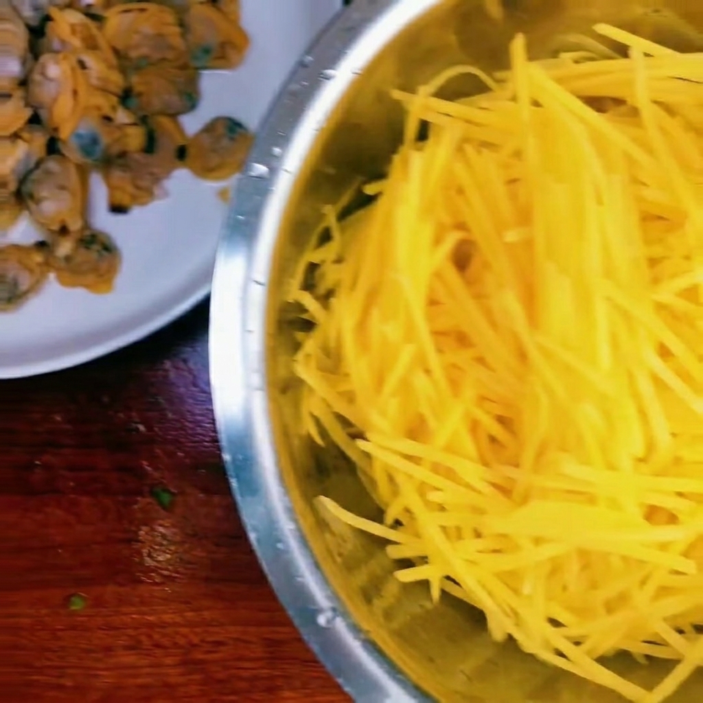 Eine Schüssel mit rohen Kartoffelstreifen, gekochtem Muschelfleisch und gehackten Frühlingszwiebeln.