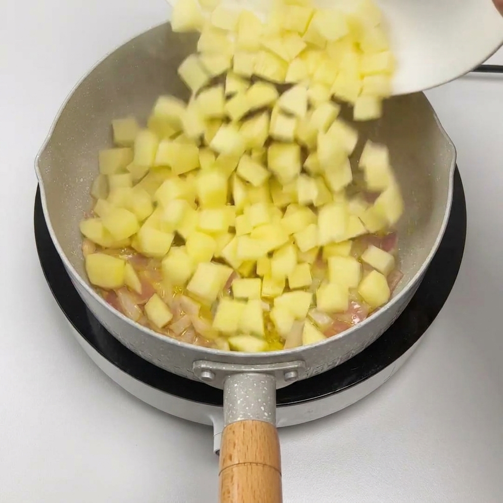 Gewürfelte Kartoffeln werden zu den angedünsteten Zwiebeln in die Pfanne gegeben.
