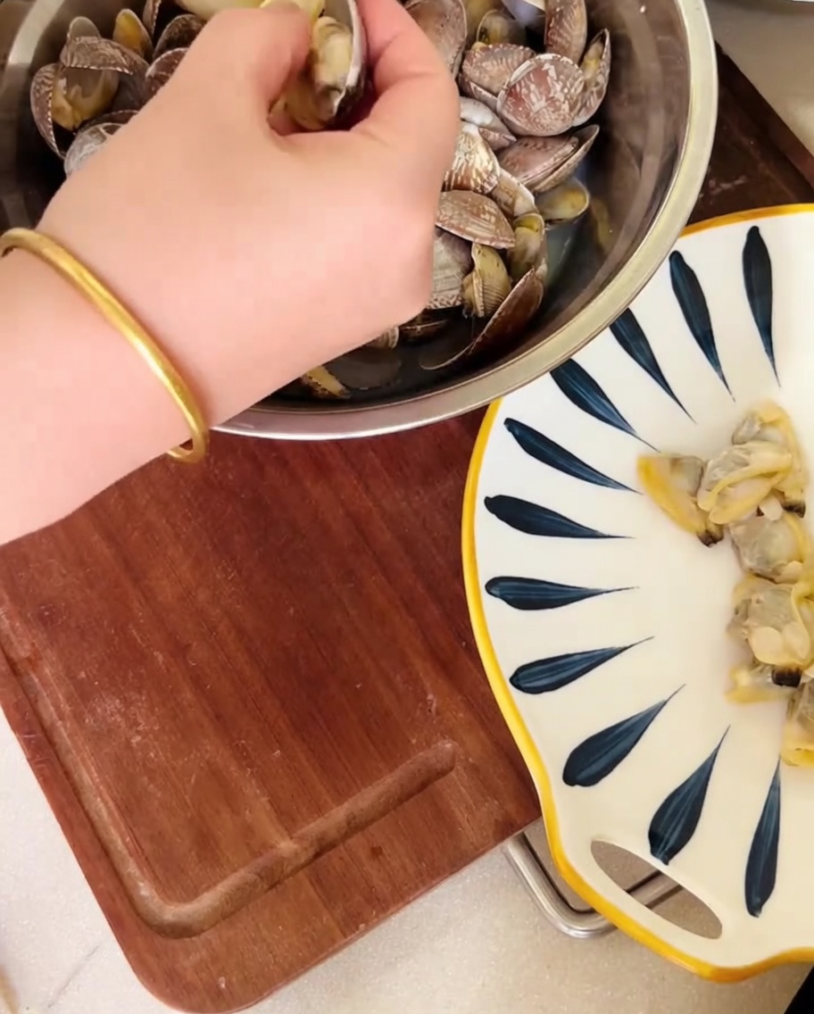 Eine Hand löst Muschelfleisch aus den Schalen über einer Schüssel, der Sud wird aufgefangen.