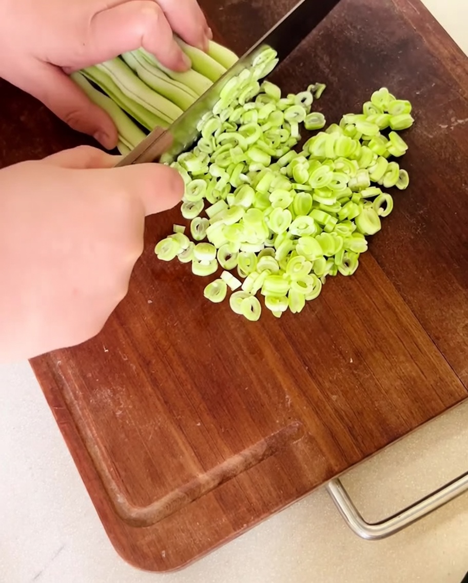 Fein gehackte grüne Bohnen auf einem Holzschneidebrett.
