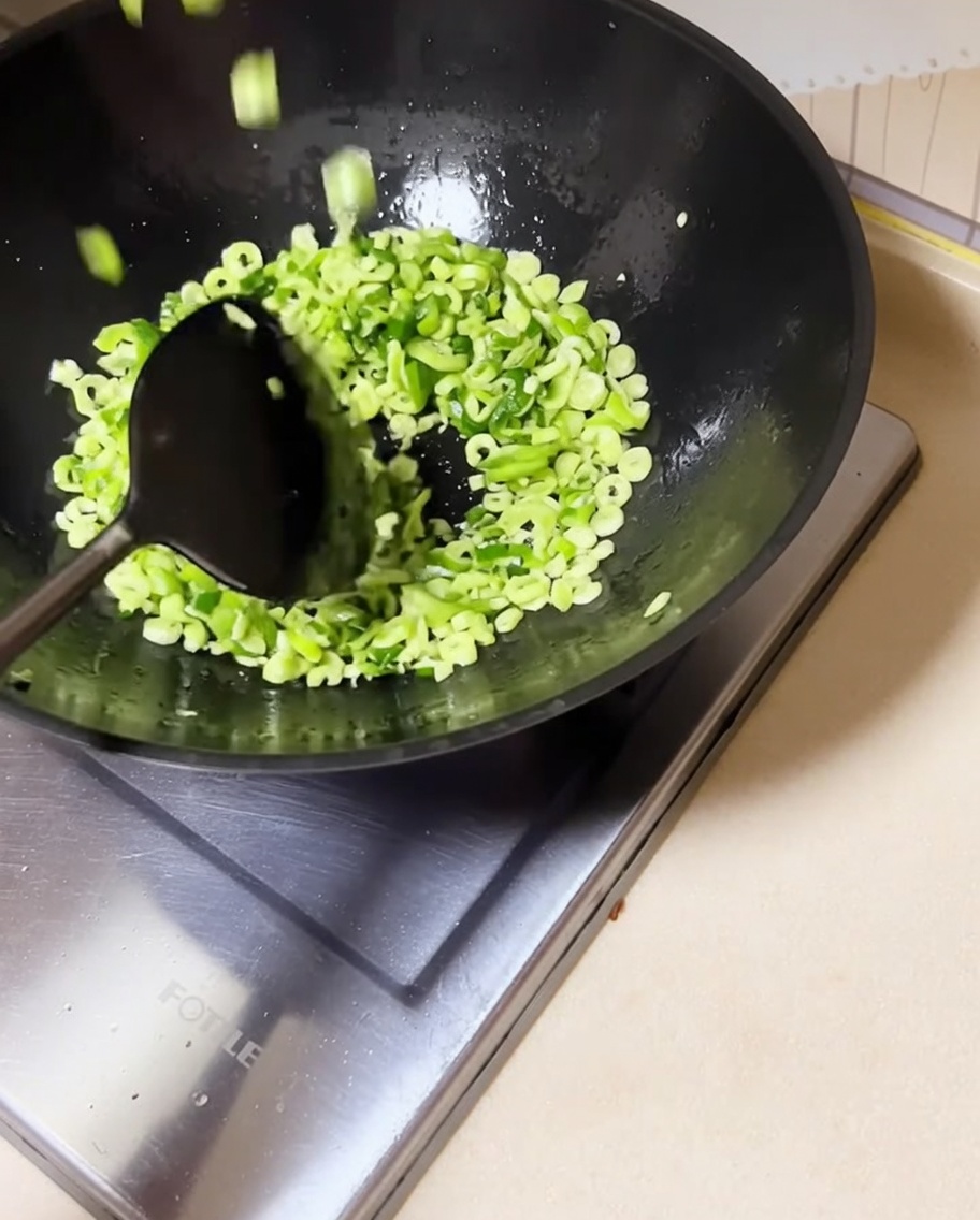 Gehackte grüne Bohnen werden mit angedünsteten Zwiebeln im Wok verrührt.